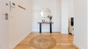 A hallway with a wooden floor, a round mirror, a small table with a vase, and a TV on a stand. - Superb Flat w/ Balcony and AC by LovelyStay (Porto)