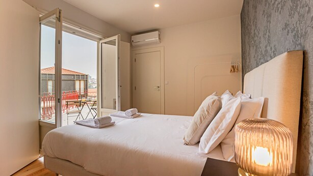 A hotel room with a large bed, a bedside lamp, and a view of the outside balcony. - Superb Flat w/ Balcony and AC by LovelyStay (Porto)