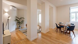 A modern dining area with a wooden table set for four, a potted plant, and a floor lamp. - Superb Flat w/ Balcony and AC by LovelyStay (Porto)