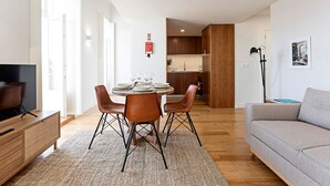 Un salon moderne avec un coin repas, un plancher en bois et un canapé gris.