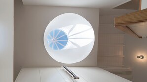 A modern room with a circular skylight, a minimalist design, and a wooden ceiling structure.