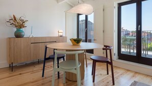A modern dining area with a round table, two chairs, a vase with dried flowers, and a view of the outside through large windows.