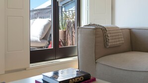 A room with a beige sofa, a window with a view of a patio, and a table with books.