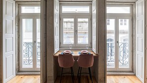 A dining area with a table set for two, two chairs, and a view of the city through large windows. - Turquoise Flat w/ AC & Balcony by LovelyStay (Porto)