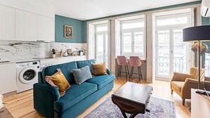 A modern apartment with a teal sofa, a wooden coffee table, and a kitchen with a washing machine. - Turquoise Flat w/ AC & Balcony by LovelyStay (Porto)
