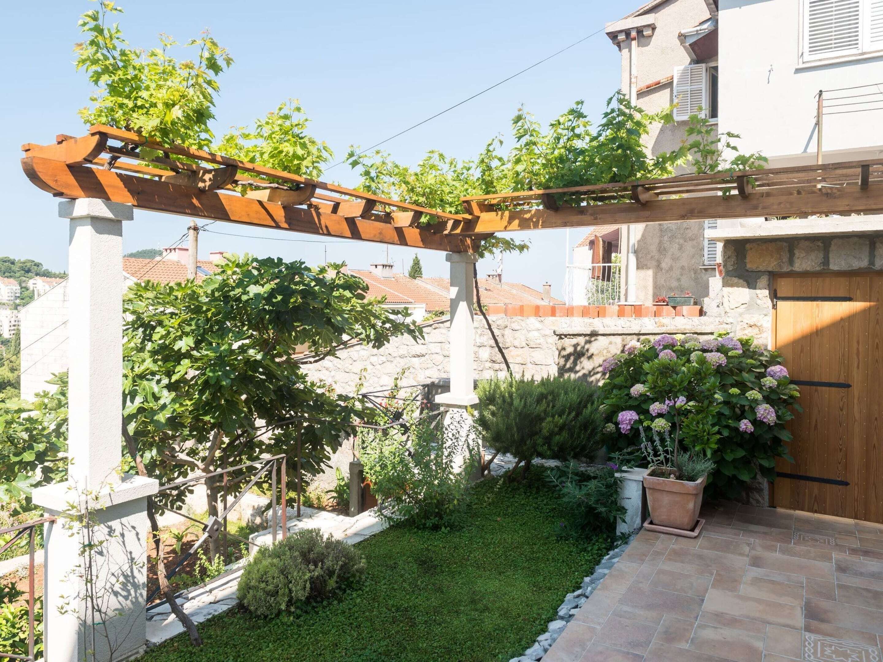 Un jardin agrémenté d’une pergola, d’un mur en pierre et d’une porte en bois.