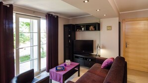 A living room with a sofa, a table, a TV, and a window with curtains. - Apartments Gaura - Comfort One-bedroom Apartment With Terrace (Dubrovnik)