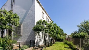 Un edificio blanco con techo inclinado, rodeado de follaje y una valla.