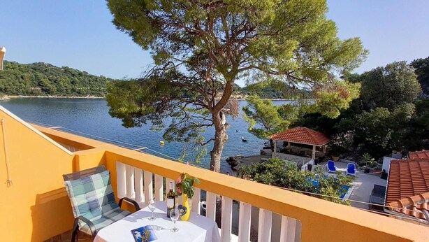 Ein Balkon mit einem Tisch für zwei Personen, mit Blick auf einen See und ein Laube.
