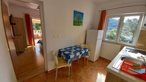 Eine kleine Küche mit Esstisch, Kühlschrank und Fenster mit Blick auf Bäume.