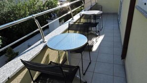 Un balcon avec une table ronde et deux chaises, une rambarde en métal et une vue sur un immeuble et de la verdure.