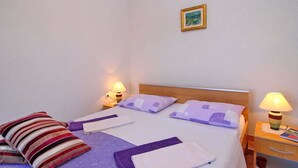 A neatly made bed with purple and white bedding, two bedside lamps, a small bedside table with a lamp, and a framed picture on the wall.