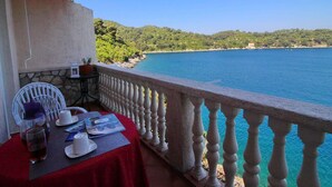 A balcony with a table set for two, overlooking a clear blue sea and a hilly landscape.
