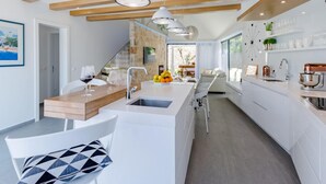 Moderni keittiö, jossa on keskeinen saareke, valkoiset kaapit ja puupalkit katossa.