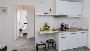 A modern kitchen with white cabinets, a wooden countertop, and a sink. There is a small stool with a decorative item on it. - Apartment Semi - One Bedroom Apartment With Terrace and Sea View (Dubrovnik)