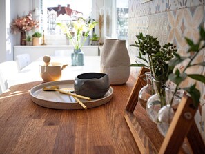 A wooden table with a ceramic bowl, a spoon, and a teapot. There are potted plants and a tiled wall in the background. - Apartment Pantarul - One Bedroom Apartment With City View (Dubrovnik)