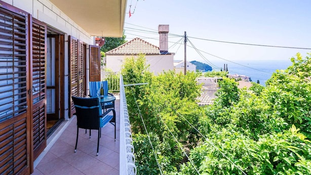 Un balcón con mesa y sillas, con vistas a un jardín y al mar.