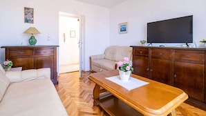 Una sala de estar con sofá, una mesa de centro de madera, televisor y aparador.