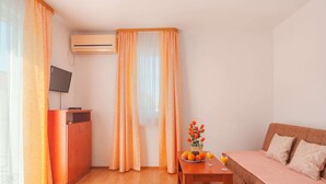 A hotel room with a wooden desk, a bed, a TV on a stand, and a window with curtains. - Apartments Island Beat - Two Bedroom Apartment With Balcony (Supetar)