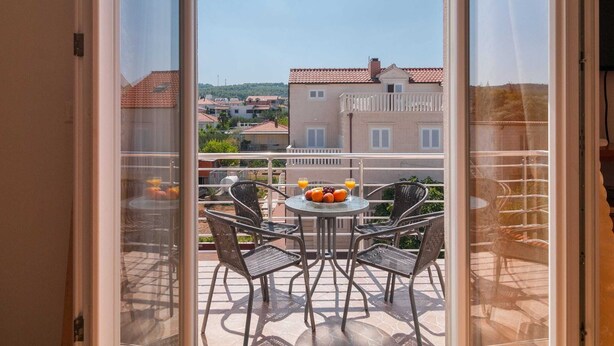 A balcony with a table and chairs, a clock on the wall, and a view of buildings in the background. - Apartments Island Beat - Two Bedroom Apartment With Balcony (Supetar)