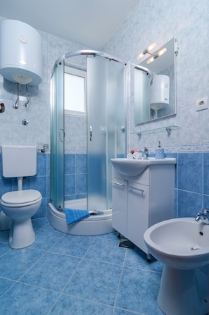 Een badkamer met toilet, douchecabine, wastafel en bidet.