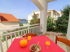 A balcony with a red tablecloth, a pitcher of orange juice, and two glasses of orange juice. - Apartments Marko Peljesac - Two Bedroom Apartment (Orebic)
