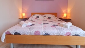 Een keurig opgemaakt bed met bloemenbedrukking, twee nachtlampjes en een schilderij aan de muur.