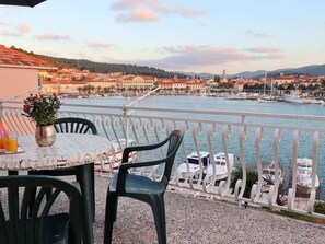 Un balcón con una mesa, sillas y vista a un río con barcos y edificios al fondo.