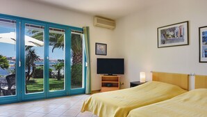 Habitación de hotel con dos camas, televisión y vista al mar a través de una puerta de cristal.