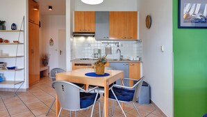 Cocina compacta con armarios de madera, una mesa de comedor con sillas y una lámpara colgante.