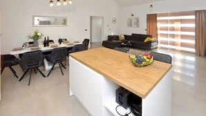 A modern kitchen with a central island, dining area with chairs, and a living area with a sofa. - Villa in Starigrad With Heated Pool (Starigrad)