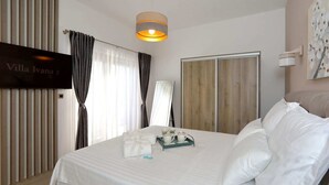 A hotel room with a bed, a bedside table with a tray of items, a mirror, a wall-mounted TV, and a window with curtains. - Villa in Starigrad With Heated Pool (Starigrad)