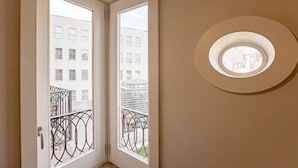 Ein Zimmer mit einer Tür zu einem Balkon mit Metallgeländern und Blick auf Gebäude.