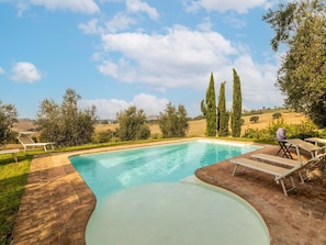 A rectangular swimming pool with a curved edge, surrounded by a brick patio. There are lounge chairs and a table on the patio. - Belvilla by OYO Villa Osimo (Osimo)