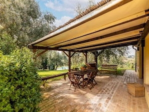 A covered patio with a brick floor, wooden furniture, and a view of a swimming pool and greenery. - Belvilla by OYO Villa Osimo (Osimo)
