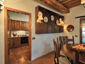 Una cocina rústica con armarios de madera, una mesa de comedor con sillas y una estantería con platos decorativos.