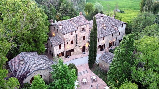 Un edificio de piedra grande con varias habitaciones y un patio con mesas al aire libre.