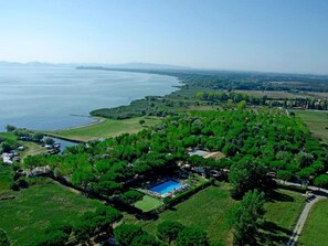 Vista aerea di una proprietà costiera con piscina, campi verdi e un porto turistico.