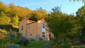A two-story building with a stone base and a beige upper section, surrounded by lush greenery and trees. - Apartment in Liguria Near Toirano Caves (Vezzi Portio)