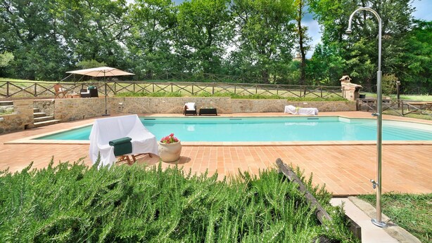A swimming pool with a stone wall and a wooden deck. There are lounge chairs and a table with a white tablecloth. - Holiday Home in Pontano With Garden (Sant'Angelo in Pontano)