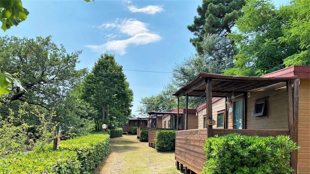 A row of wooden cabins with a gravel path between them, surrounded by greenery and trees. - Belvilla by OYO Lovely Bungalow With a Shared Pool (Capraia e Limite)