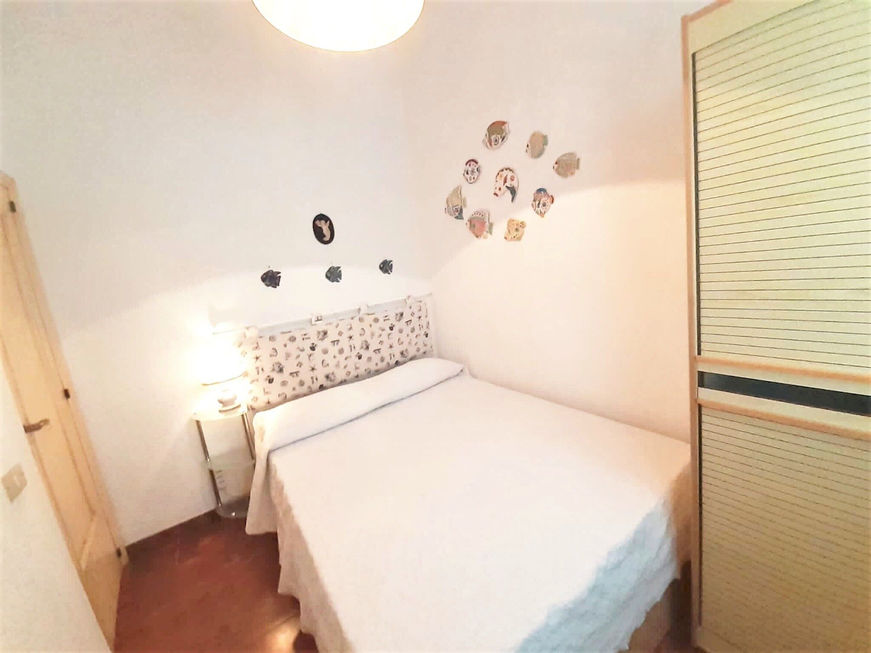 A small, neatly arranged bedroom with a single bed, a bedside table with a lamp, and a wall decorated with small animal stickers.