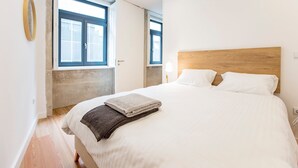 Ein Schlafzimmer mit einem großen Bett, zwei Fenstern und einem Holz-Kopfende.