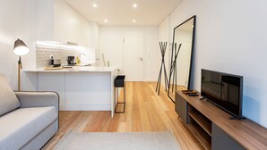 Ein modernes Wohnzimmer mit Sofa, Fernseher, Couchtisch und einer Küchenzeile inklusive Arbeitsplatte und Geräten.