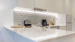 Eine moderne Küche mit weißen Schränken, einer Marmorarbeitsplatte, einem Einbauofen, einer Kaffeemaschine und einem Wasserkocher.