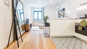 Eine moderne Küche mit großem Fenster, einem Essbereich mit weißem Tisch und Stühlen sowie einer kleinen Sitzecke mit einer Couch.