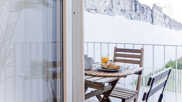 Una mesa de madera con un plato de comida y un vaso de jugo de naranja en un balcón con vistas a un acantilado rocoso.