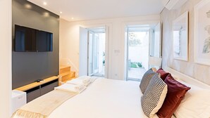 Un dormitorio moderno con una cama grande, un televisor de pantalla plana montado en la pared, una escalera de madera y un door de vidrio corredera que da a un balcón.