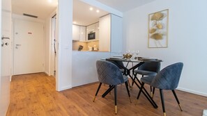 Un espace repas moderne avec une table ronde, deux chaises grises à revêtement rembourré et une décoration minimaliste comprenant une œuvre d’art encadrée accrochée au mur.