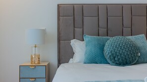 Un lit bien fait, avec une tête de lit grise, une table de chevet avec une lampe et deux coussins décoratifs.